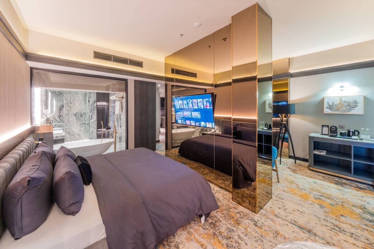 Een moderne hotelkamer met een groot bed, een televisie, een bureau en een badkamer met een bad.