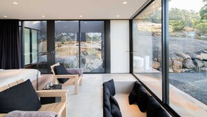 Een moderne kamer met een groot raam, een bed, een houten stoel en een klein tafeltje met een kopje.