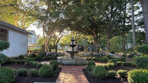 A garden with a central fountain, surrounded by trimmed bushes and trees.