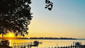 A waterfront scene with a dock and boats, trees, and a sunset.