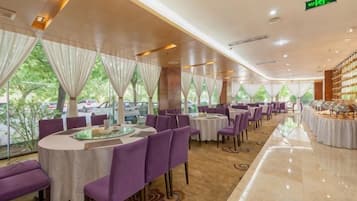 A restaurant with round tables, purple chairs, and a view of parked cars outside.