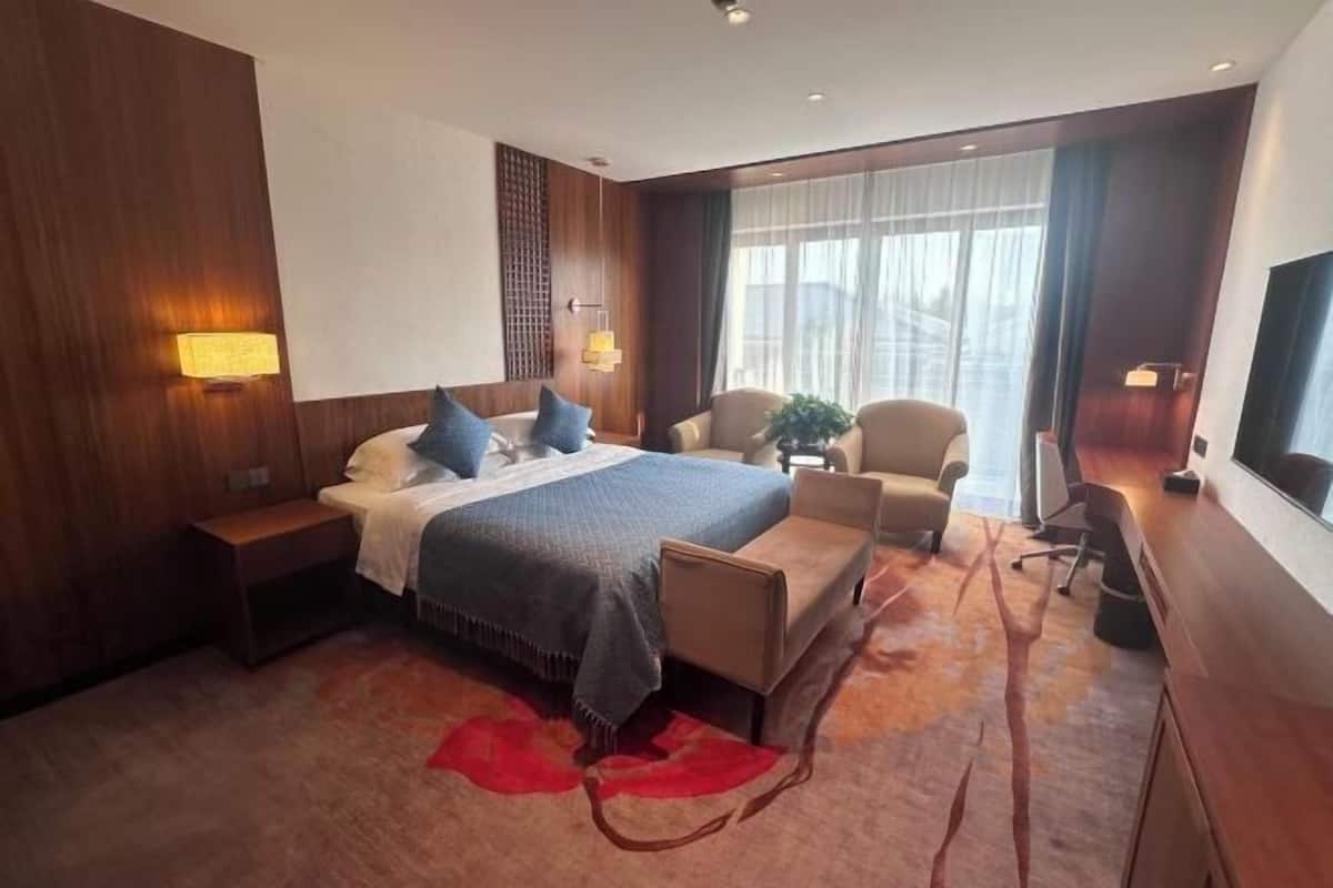 A hotel room with a bed, a desk, a chair, a small table, and a large window.