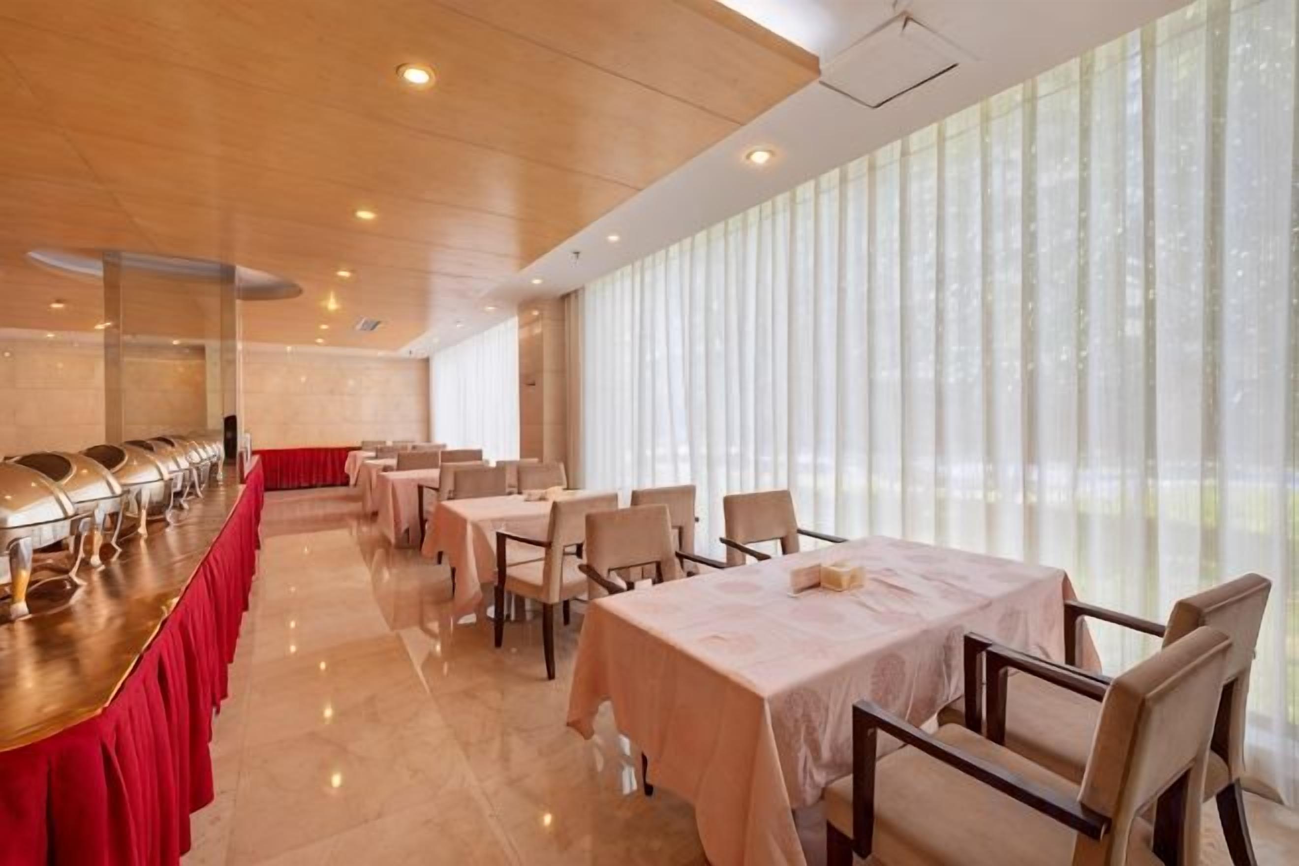 A dining area with tables and chairs, a buffet line, and large windows.