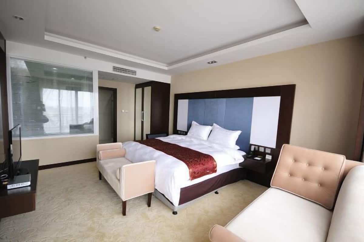 A hotel room with a large bed, a sofa, a TV, and a desk.