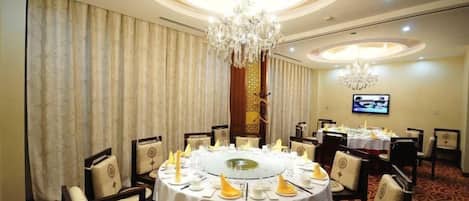 A round dining table with chairs, a chandelier, and a television on the wall.