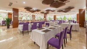Un restaurant avec des tables rondes, des chaises violettes et une vue sur la verdure grâce à de grandes fenêtres.