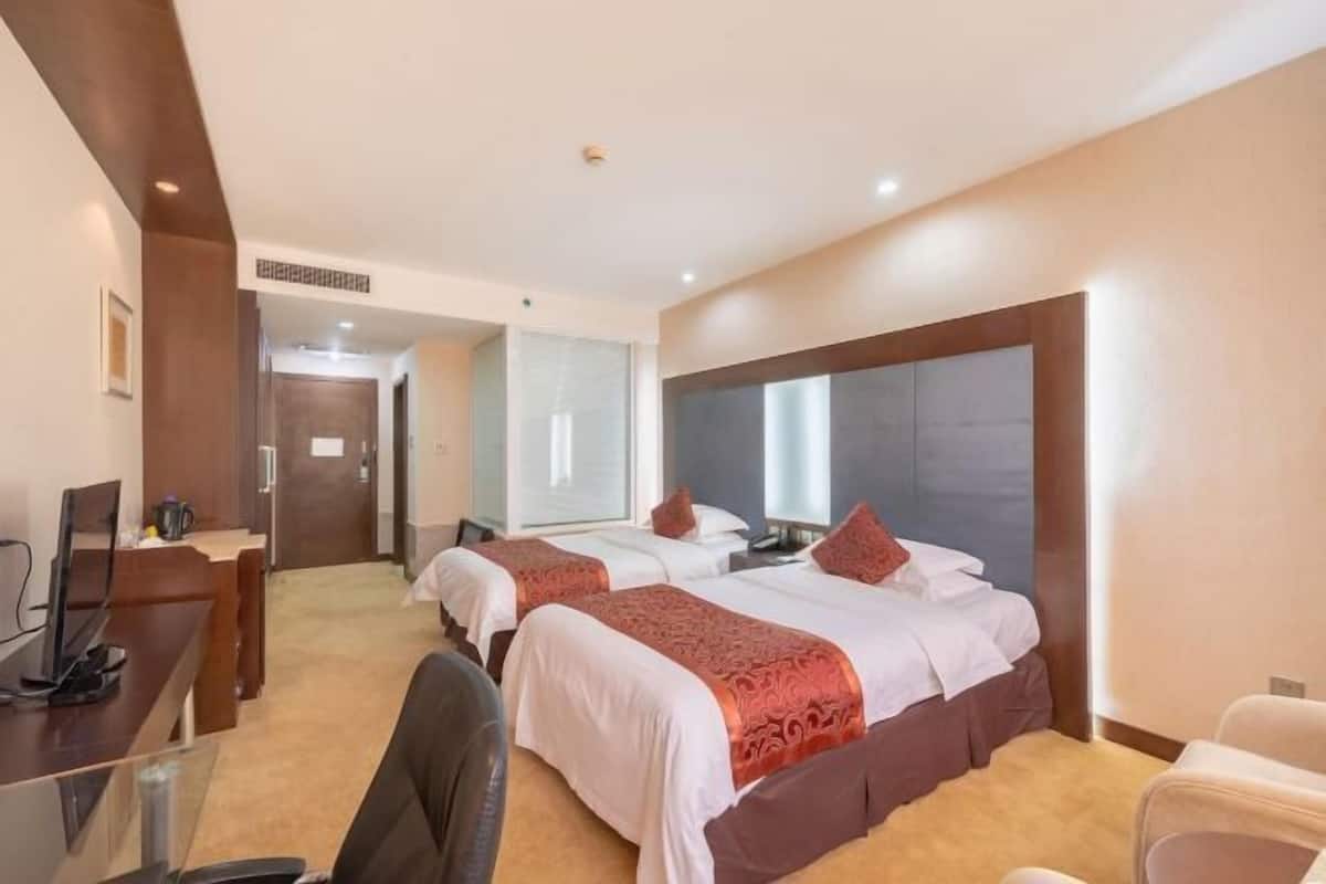 A hotel room with two beds, a desk, a chair, and a television.
