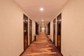 Un pasillo de hotel con puertas a ambos lados, piso de madera y una lámpara en el techo.