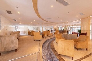 Een ruime, moderne lounge met gebogen zitplaatsen, een opvallend decoratief element en uitzicht op het interieur van het schip.