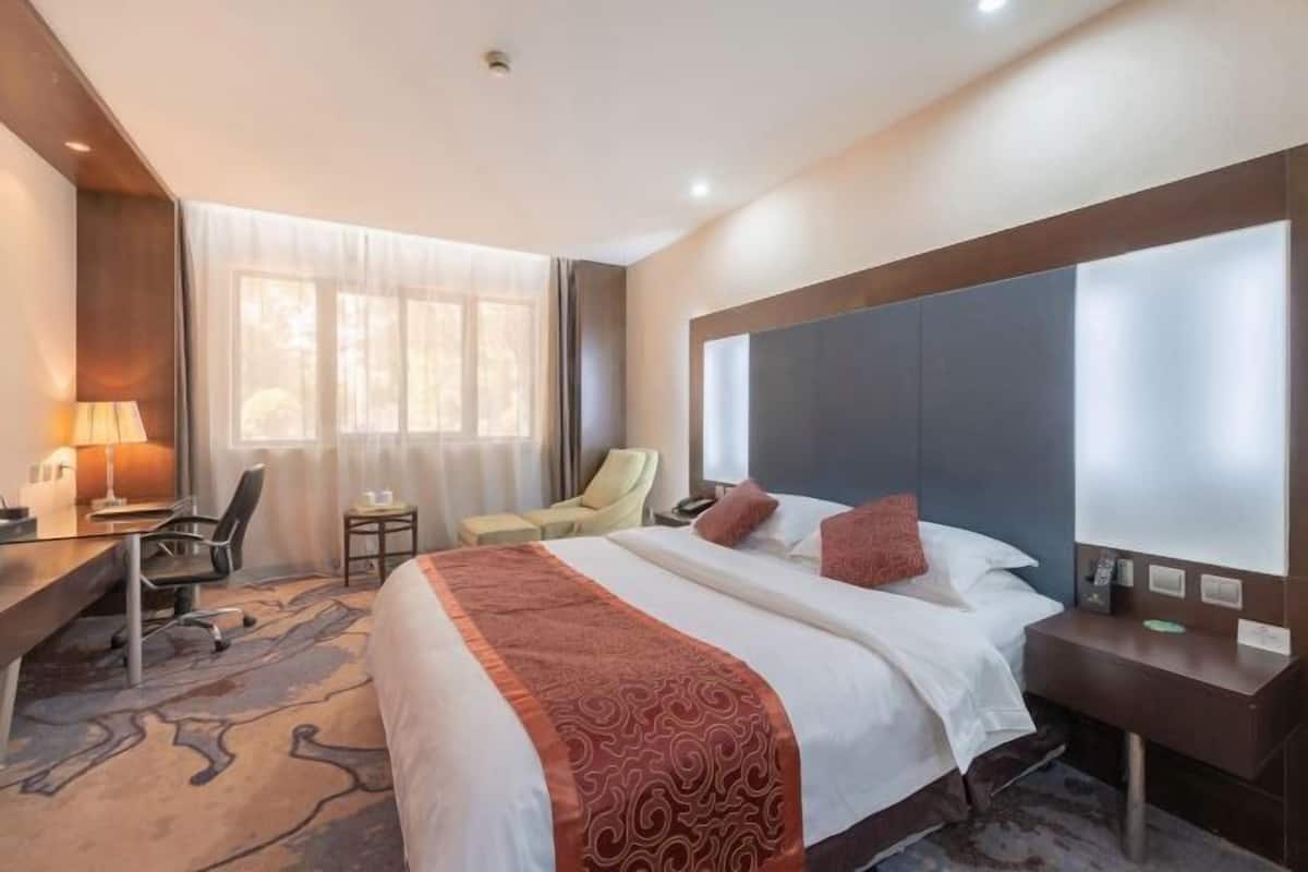 A hotel room with a large bed, a desk, a chair, a small table, and a window with curtains.