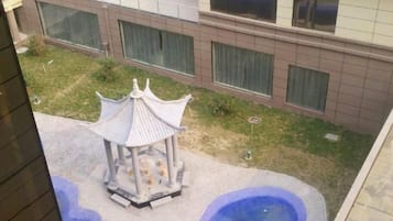 A courtyard with a traditional pavilion, a small water feature, and a building with large windows in the background.