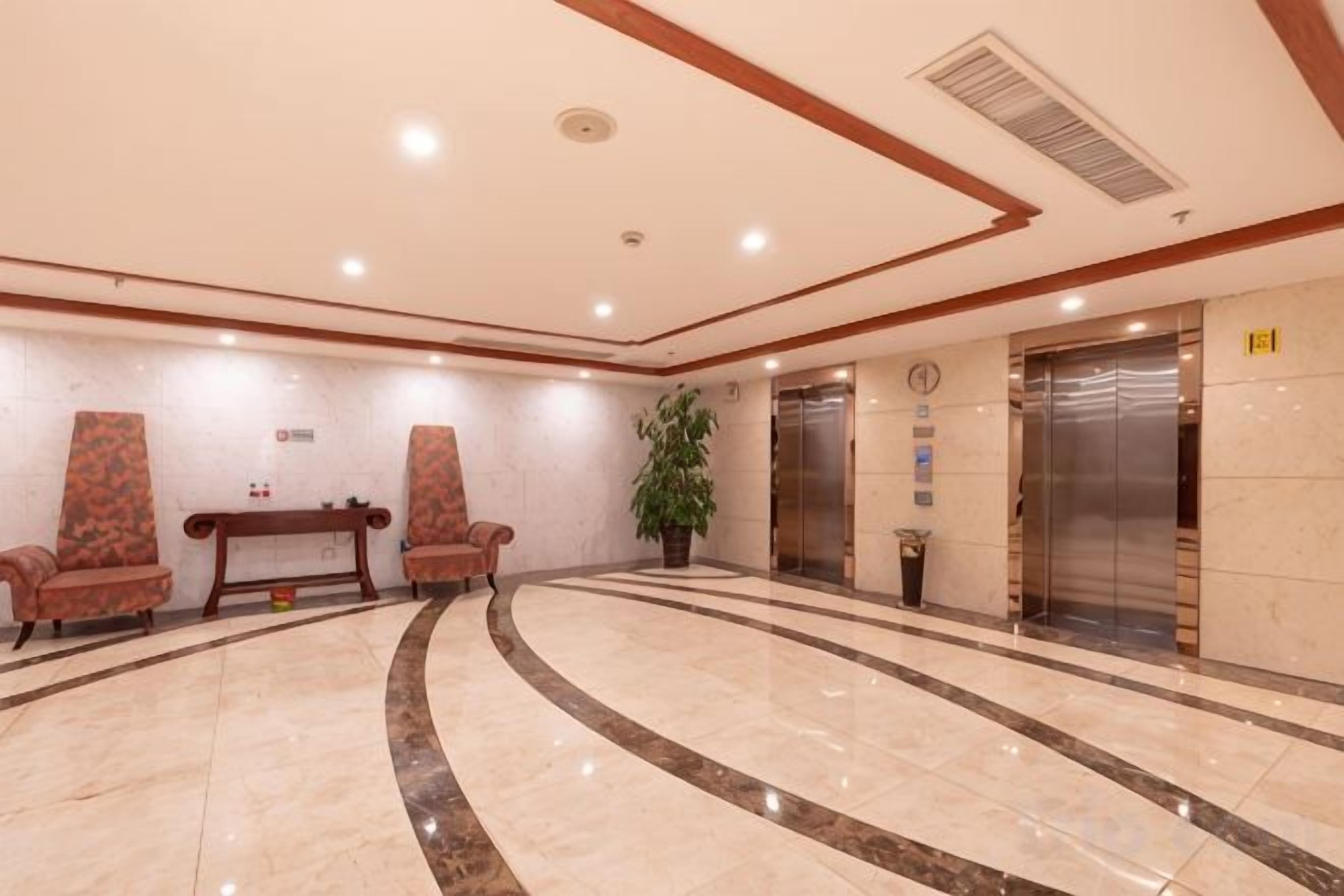 A lobby with a marble floor, two armchairs, a table, a potted plant, and an elevator.