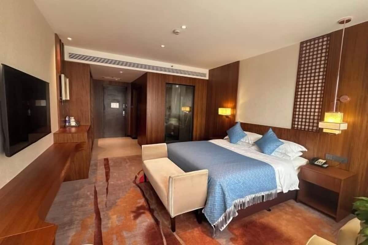 A modern hotel room with a bed, bedside tables, a TV, and a large mirror.