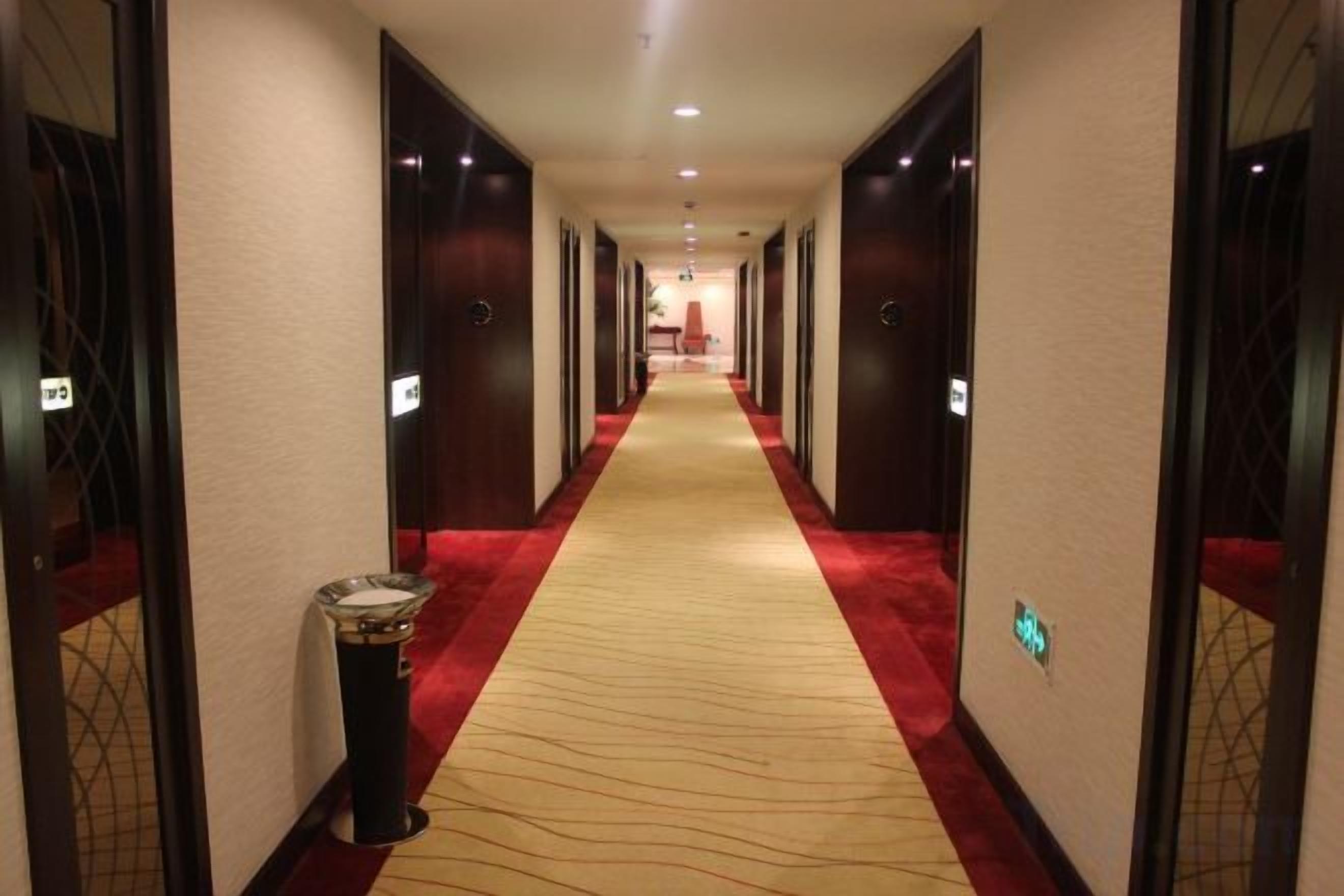 A hotel hallway with carpeted floors, doors on both sides, and a trash bin on the left.