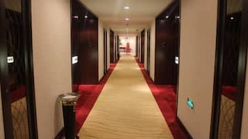 A hotel hallway with carpeted floors, doors on both sides, and a trash bin on the left.