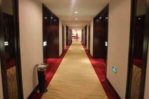 Een hotelgang met vloerbedekking, deuren aan beide zijden en een afvalbak aan de linkerkant.