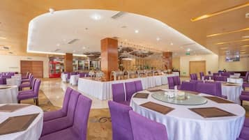 A hotel dining area with round tables and purple chairs, a central bar area, and a modern ceiling design.