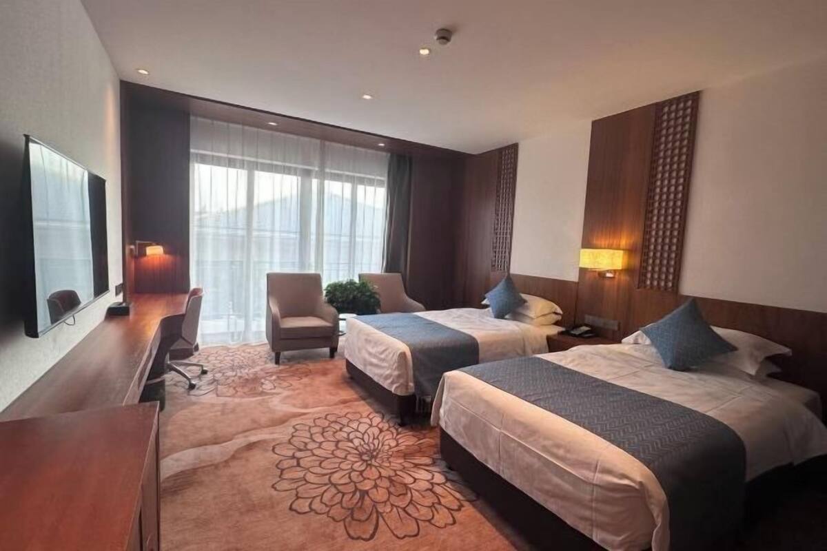 A hotel room with two beds, a desk, a chair, and a large window with curtains.