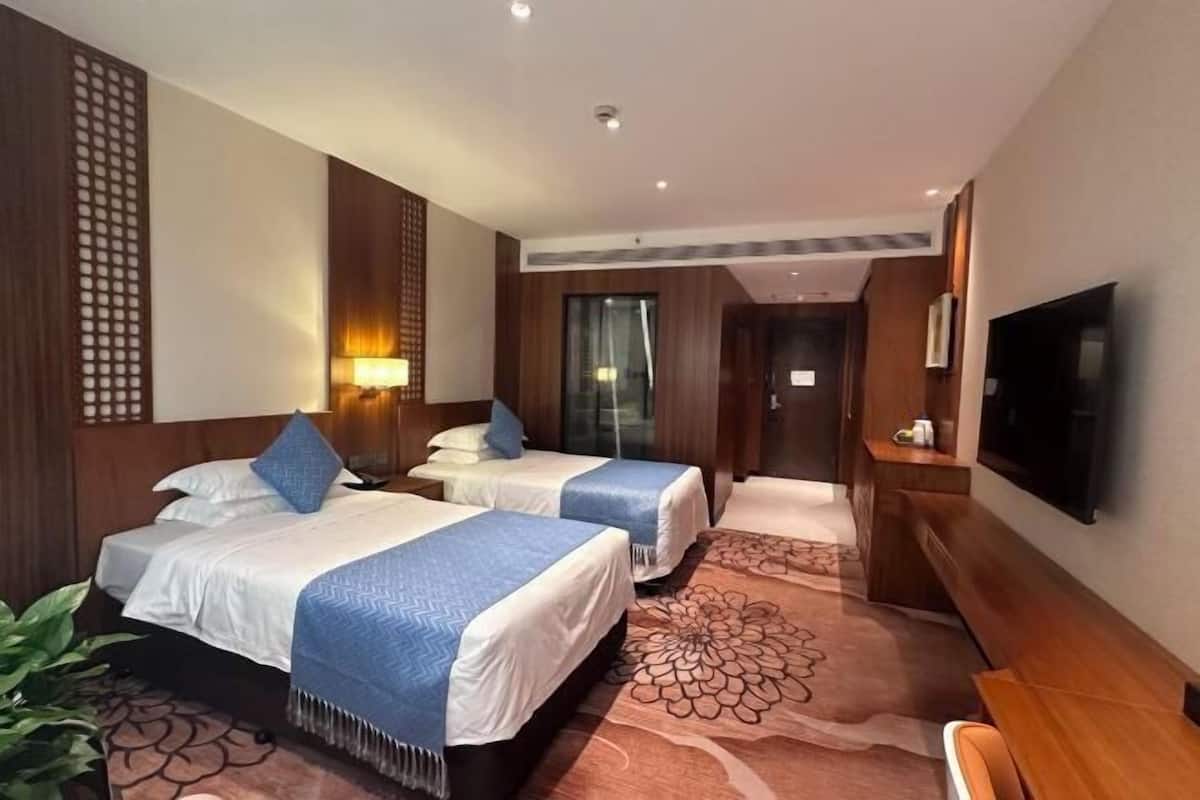 A hotel room with two beds, a TV, a desk, and a large window.