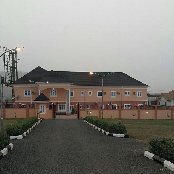 A large, multi-story building with a symmetrical facade, a central entrance, and a paved driveway leading to the entrance. - Silicon Valley Resort (Enugu)