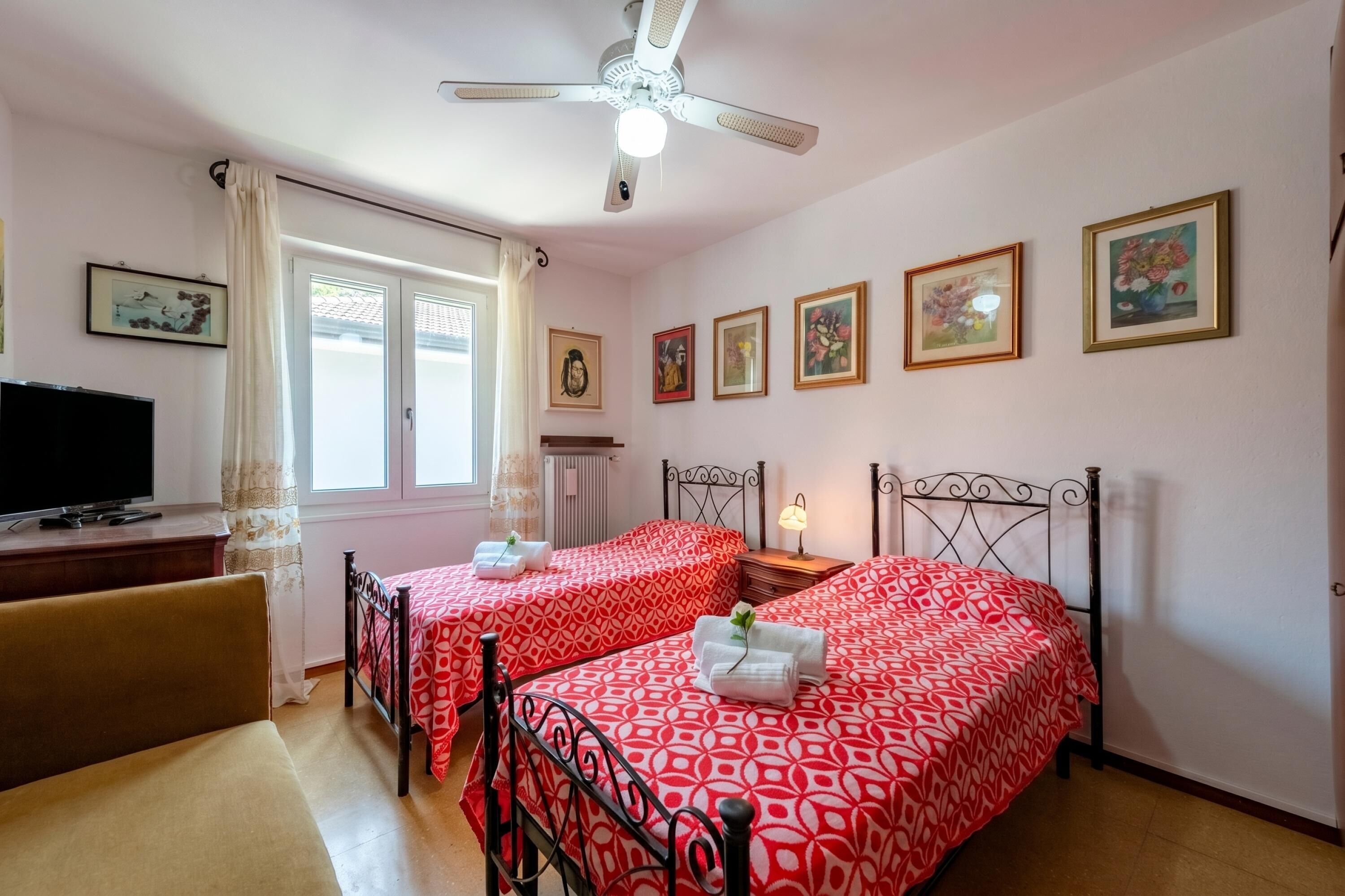 A hotel room with two beds, a TV, a ceiling fan, and several framed pictures on the wall.