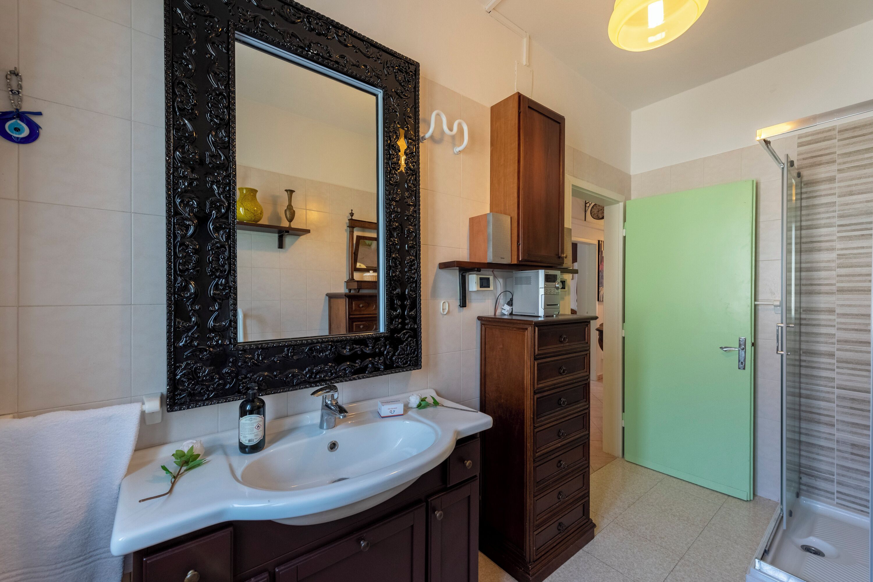 A bathroom with a white sink, a large mirror with a decorative frame, a wooden cabinet, and a green door.