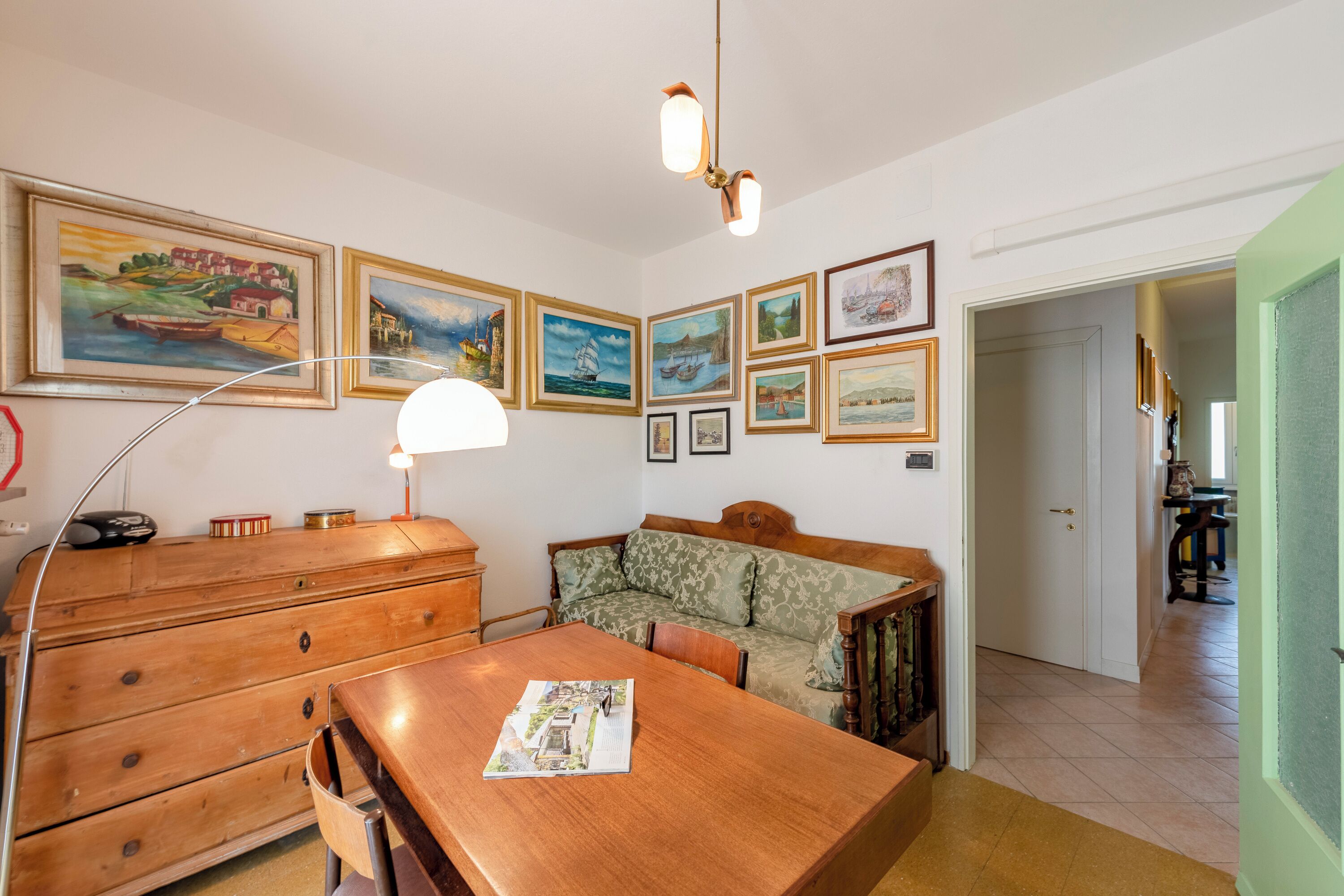 Et spiseområde med et træbord, en sofa og en lampe. Tavler med billeder hænger på væggen.