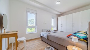 Een slaapkamer met een bed, een bureau, een stoel, een rond tapijt en een raam met uitzicht op groen.