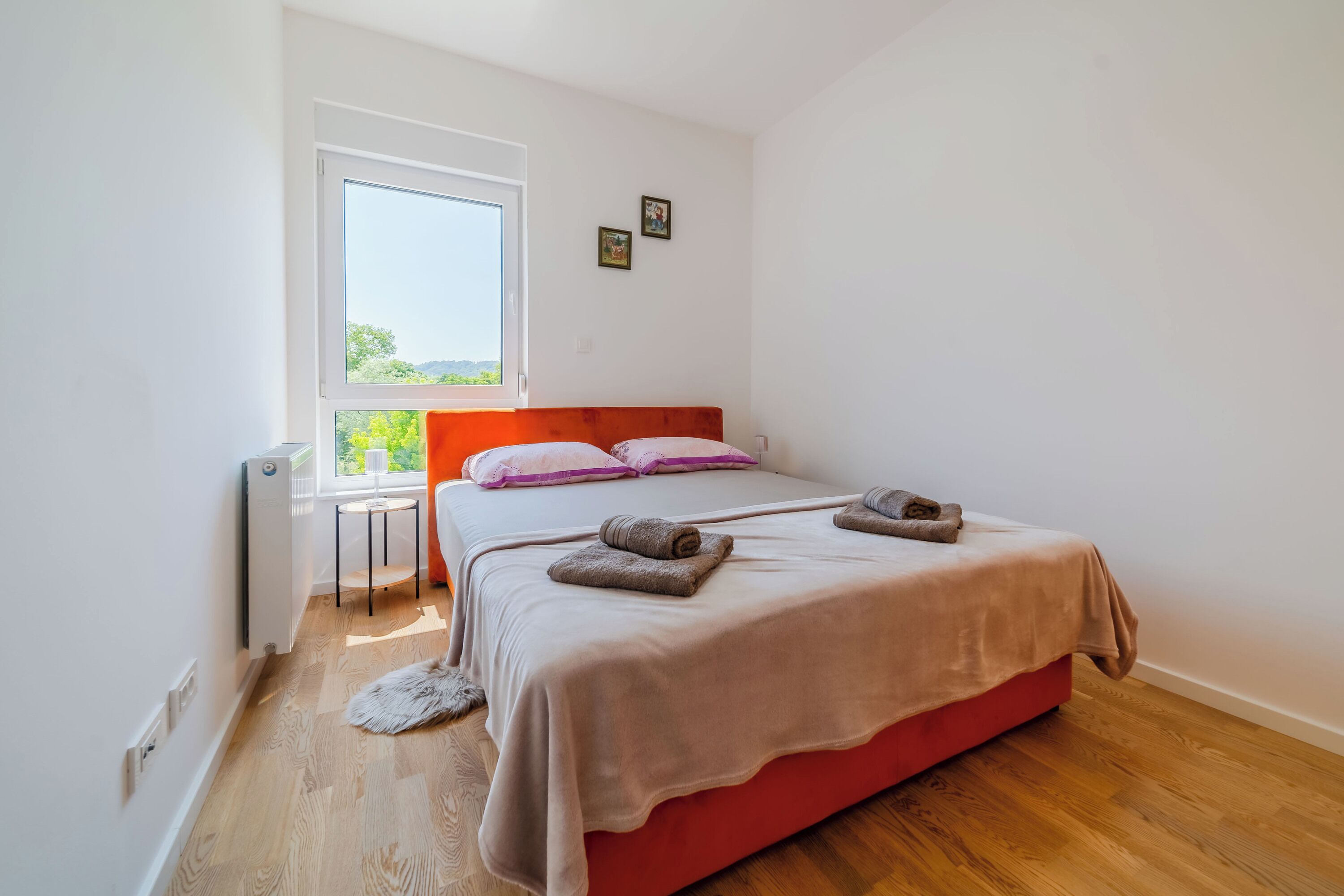 A bedroom with a bed, a window, a radiator, and a small table.