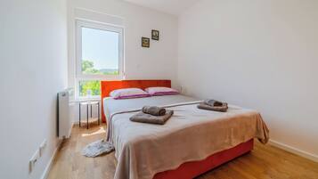 A bedroom with a bed, a window, a radiator, and a small table.