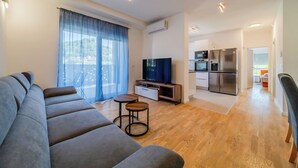 Een moderne woonkamer met een grijze bank, een televisie en een keuken met een koelkast en oven.