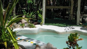 Une piscine bordée de blanc, entourée de rochers et de plantes.