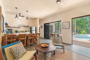 A modern kitchen with wooden cabinets and a dining area with a round table and chairs. - Chemuyil Jungle Villa - 2BR and Plunge Pool (Ciudad Chemuyil)