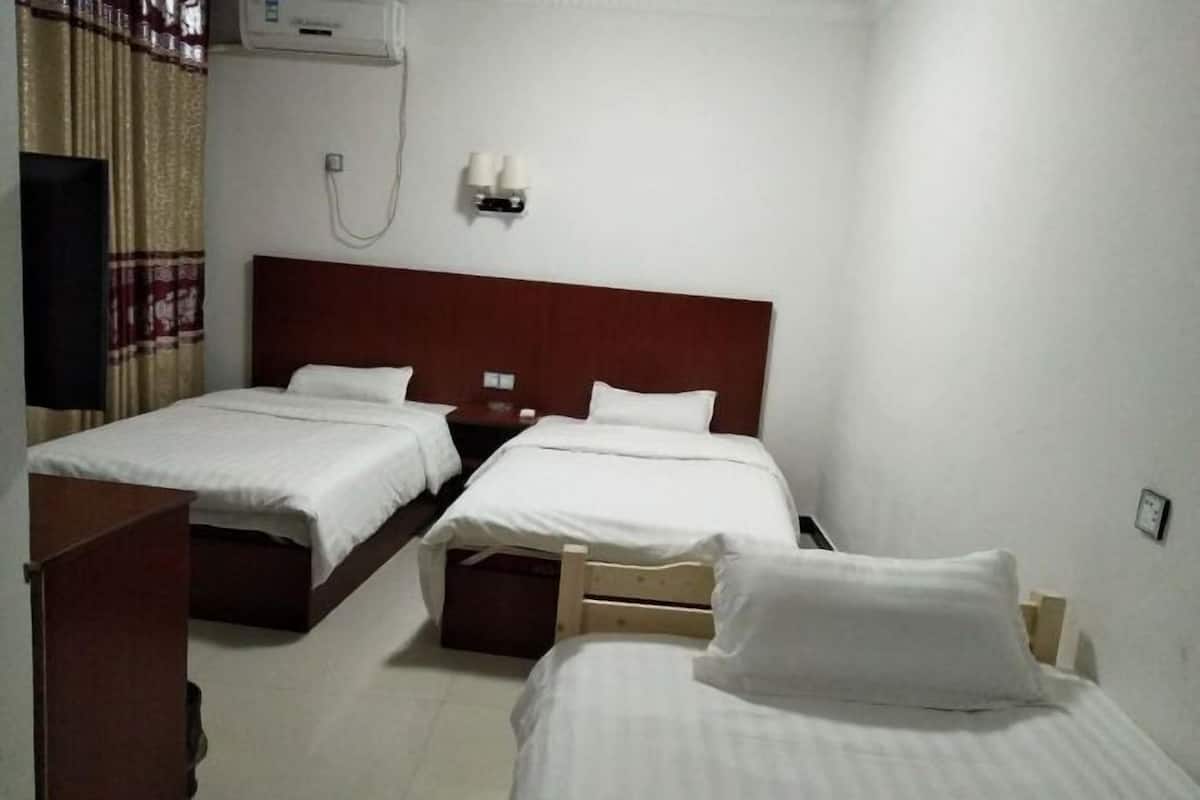 Habitación de hotel con dos camas individuales, cabecero de madera, mesita de noche, unidad de aire acondicionado y lámpara de pared.