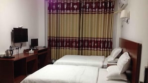 Una habitación de hotel con dos camas, un escritorio con televisor y una ventana con cortinas.