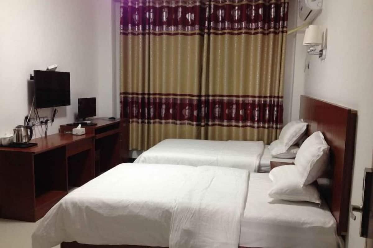 Una habitación de hotel con dos camas, un escritorio con televisor y una ventana con cortinas.