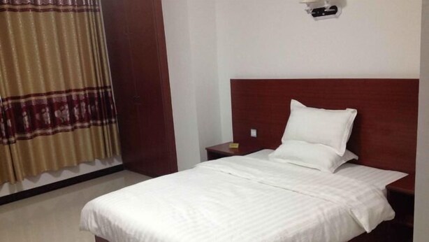 Una habitación de hotel con cama, mesita de noche, lámpara y cortina.