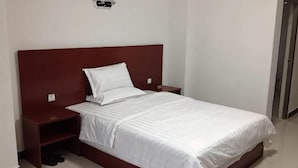 Una cama individual con cabecera de madera, una colcha blanca y una mesita de noche con una lámpara.