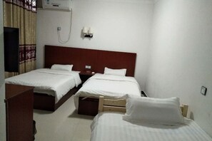 Une chambre d’hôtel avec deux lits, une tête de lit en bois, une table de chevet, un climatiseur fixé au mur et un rideau.