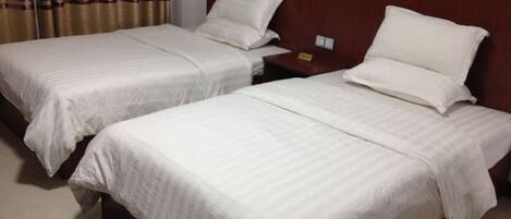 Dos camas individuales con cabeceros de madera y ropa de cama blanca en una habitación de hotel.