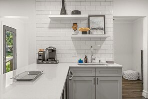 Una cocina moderna con azulejos tipo metro blancos, una cafetera y un lavamanos.
