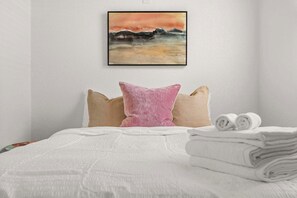 A neatly made bed with a white duvet, a pink pillow, and two beige pillows. There is a framed painting of a landscape on the wall above the bed. - SoHo Oasis - Stunning Home In Heart of SoHo (Tampa)