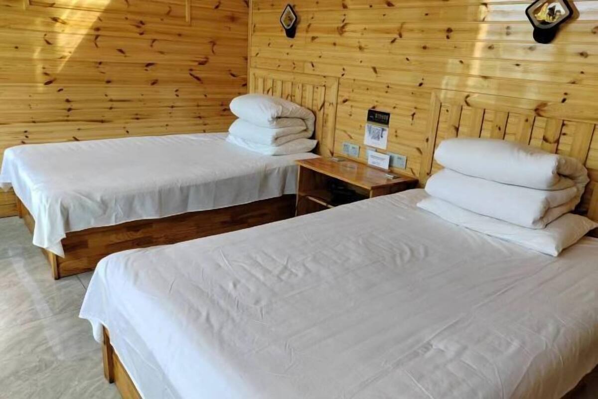 Una habitación con dos camas individuales, paredes de madera, una mesita de noche de madera y un aplique fijado a la pared.