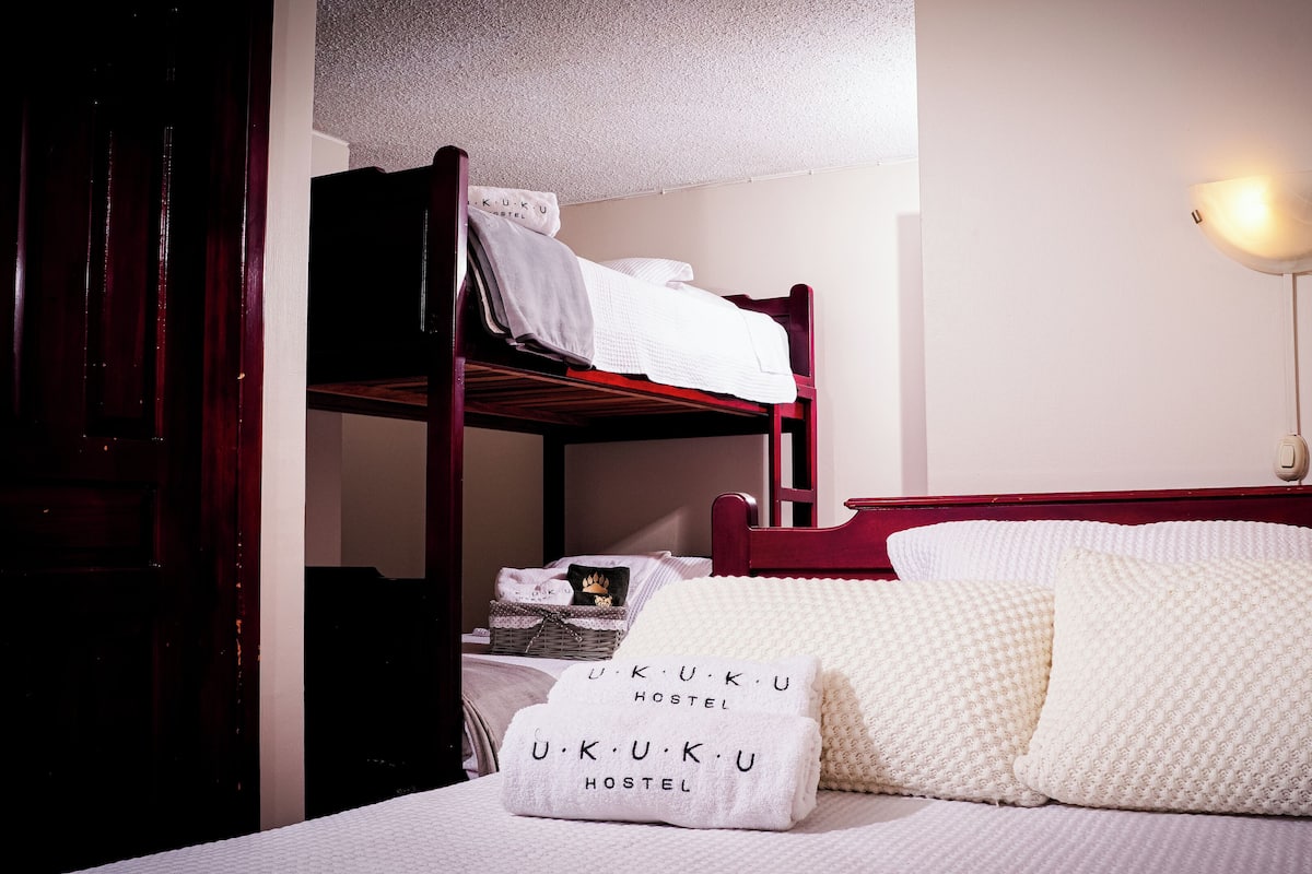 A bunk bed with a white mattress and pillows, a bedside table with a lamp, and a wall with a textured pattern.