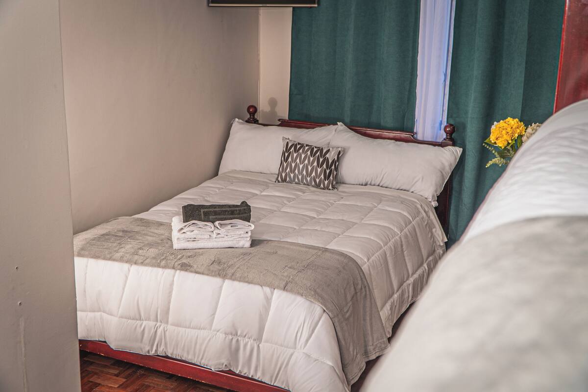 A neatly made bed with a quilted bedspread, a folded towel, and a patterned pillow.