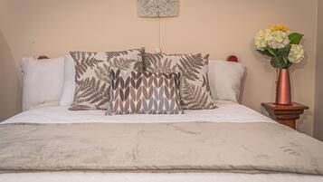 A neatly made bed with patterned pillows, a bedside table with a vase of flowers, and a wall-mounted lamp.