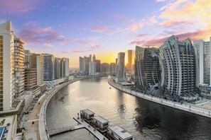 A waterfront cityscape with modern high-rise buildings, a curved river, and a pedestrian walkway along the riverbank.