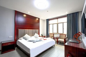 A hotel room with a large bed, a desk, a chair, and a television.