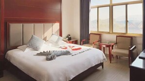 Une chambre d’hôtel avec un grand lit, une petite table, deux chaises et une vue sur les montagnes par la fenêtre.