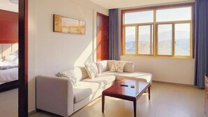 Une chambre d’hôtel moderne dotée d’une grande fenêtre donnant sur la ville, d’un canapé, d’une petite table et d’un lit avec une tête de lit en bois.